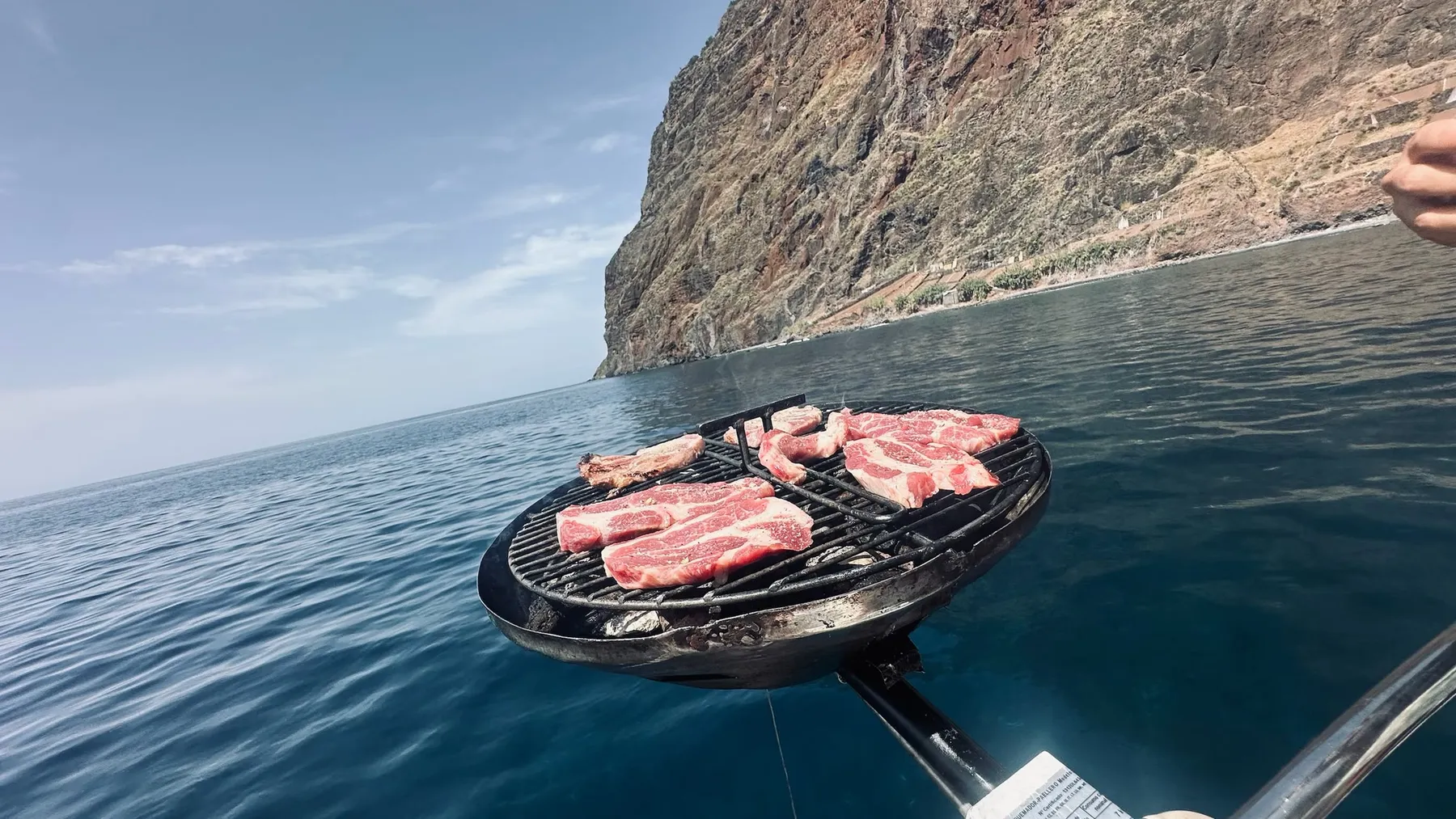 Steaks on the grill on deck, with sea cliffs behind